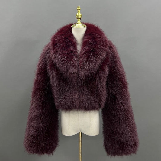 A plush, cropped fur jacket in a deep burgundy or plum shade, displayed on a cream-colored mannequin torso with a gold finial against a solid gray background.
