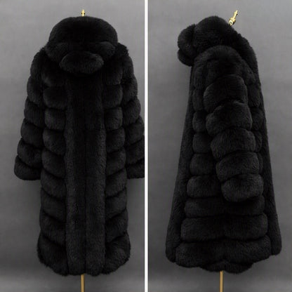 A long black fur coat displayed on a mannequin against a dark gray background, shown from the back on the left and side on the right. The coat features a large plush hood with a matching pom-pom detail and horizontal padded paneling.